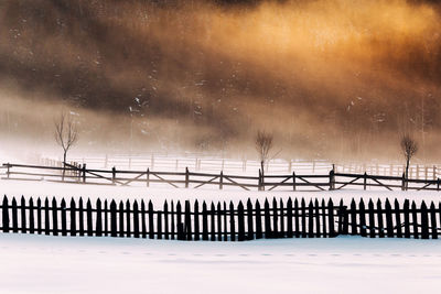 Fences on snow covered field during sunset