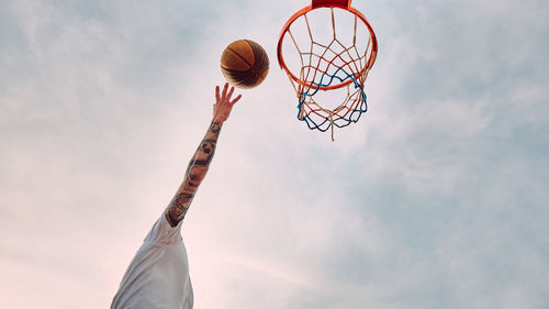 Hand of man throwing basketball to the basket hoop. bottom up view of basketball hoop and ball