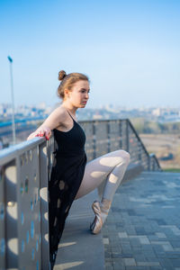 Young woman looking away while standing on railing against sky