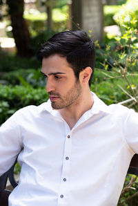 Young man looking away while standing against plants