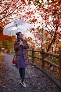 Full length of woman holding umbrella while standing on road in park during autumn