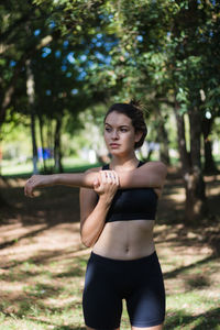 Teenage girl stretching hands looking away while exercising in park