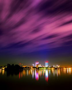 Illuminated city by river against sky at night