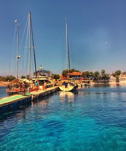 Sailboats moored at harbor against blue sky