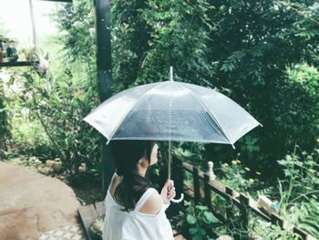 Rear view of woman with umbrella against trees