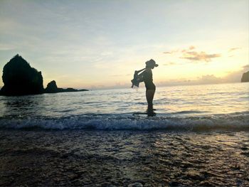 Silhouette man standing on beach against sky during sunset