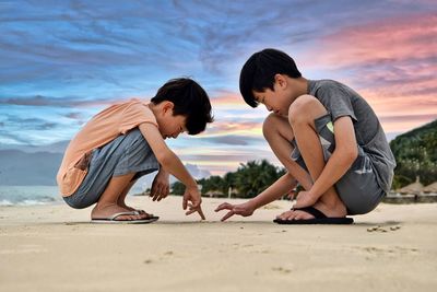 Side view of friends playing on beach against sky