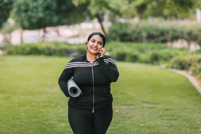 A young indian woman with a sports mat in her hands is walking from a workout in the fresh air