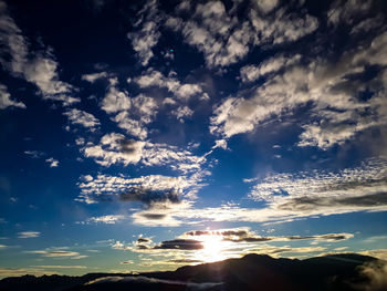 Low angle view of sunlight streaming through clouds