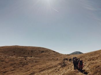 Rear view of hikers walking on mountain against sky during sunny day