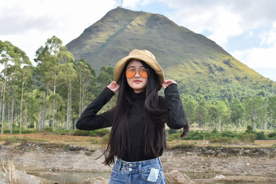 Portrait of beautiful young woman standing against mountain