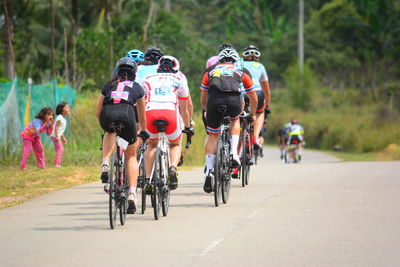 People riding bicycles on road against trees