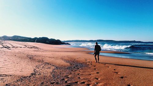 Man walking at beach against clear blue sky