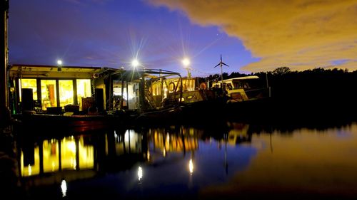 Illuminated buildings by lake against sky at night