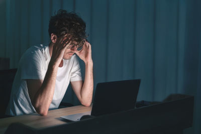 Depressed man looking at laptop while sitting in darkroom