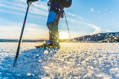 Low section of person skiing on snow covered field against sky