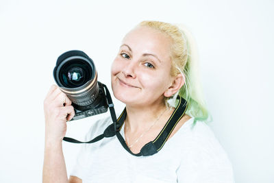 Close-up portrait of smiling woman holding camera against white background
