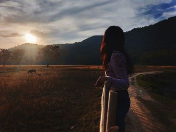 Woman standing on field against sky during sunset