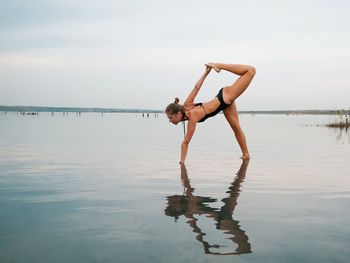 Young woman exercising while standing in sea against sky