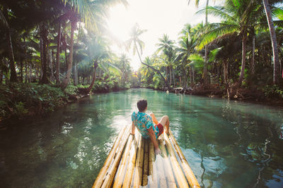 Rear view of man sitting on wooden raft in river
