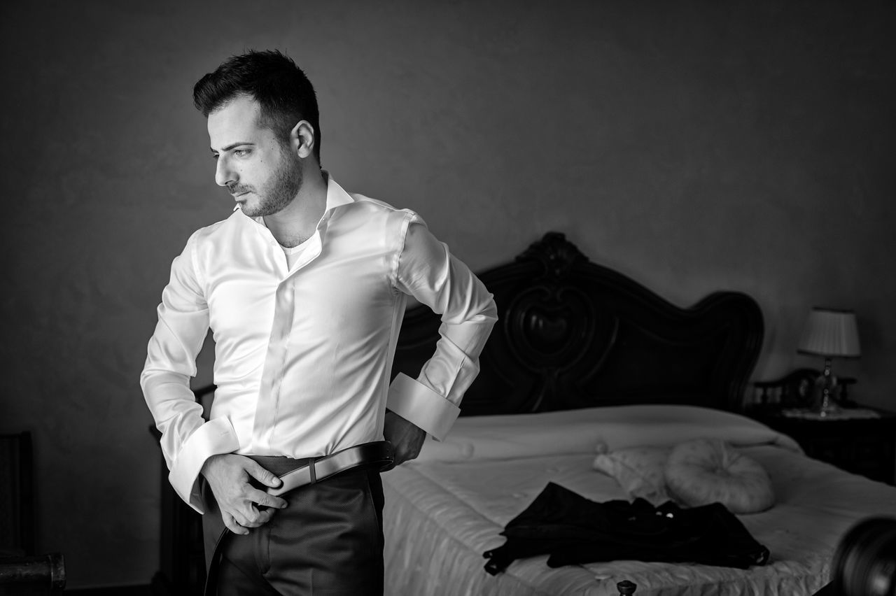 YOUNG MAN LOOKING AT CAMERA WHILE STANDING AGAINST WALL