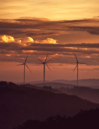 Silhouette wind turbines on land against sky during sunset