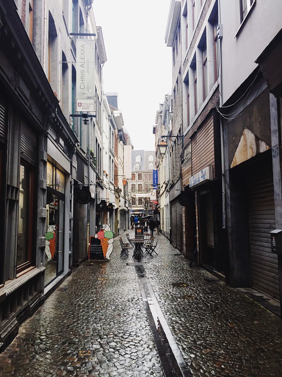 WET STREET AMIDST BUILDINGS AGAINST SKY DURING RAINY SEASON