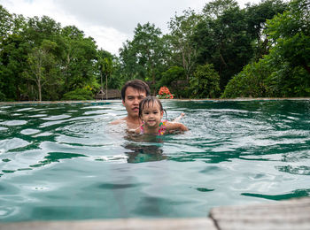 Father and daughter swimming in pool against forest