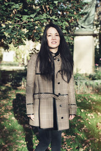 Beautiful middle-aged japanese woman in stylish coat in autumn park, smiling. sunlight, copy space