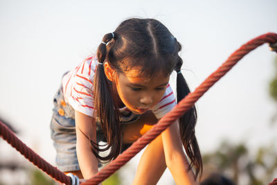 Girl climbing on jungle gym against clear sky