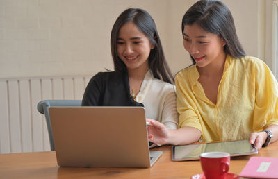 Smiling young woman using phone while sitting on table