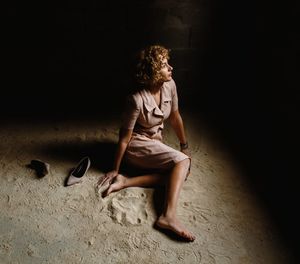 Side view of woman looking away while sitting on floor in darkroom