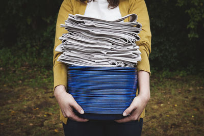 Midsection of woman holding stacked of plates and napkins at backyard