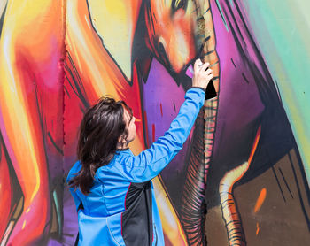 Woman standing on multi colored graffiti on wall