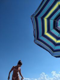 Woman standing by parasol against blue sky