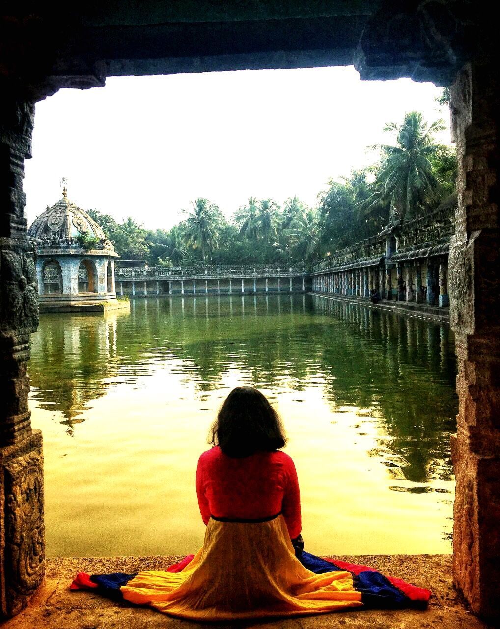 REAR VIEW OF WOMAN SITTING ON BRIDGE AGAINST LAKE