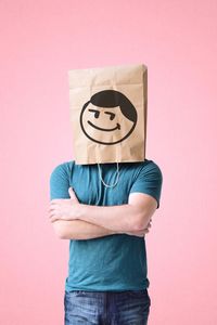 Man standing wearing paper bag anthropomorphic face against pink background