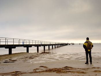 Rear view of man standing on pier over sea against sky