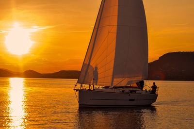 People on boat in sea against orange sky during sunny day