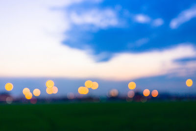 Defocused image of illuminated lights on field against sky during sunset