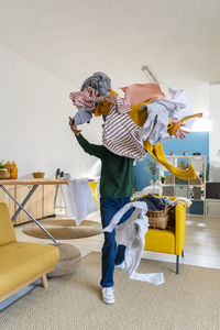 Young woman throwing clothes in living room at home