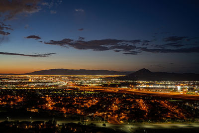 High angle view of illuminated city by sea against sky at sunset