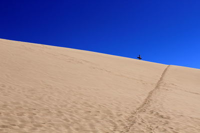 Mid distance of person walking on sand against clear blue sky