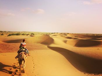 Woman sitting on sand dune in desert against sky