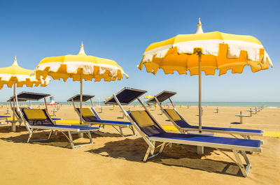 Lounge chairs and parasols on beach against clear sky