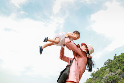 Low angle view of mother carrying daughter against sky