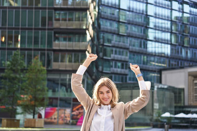 Portrait of woman with arms raised standing in city