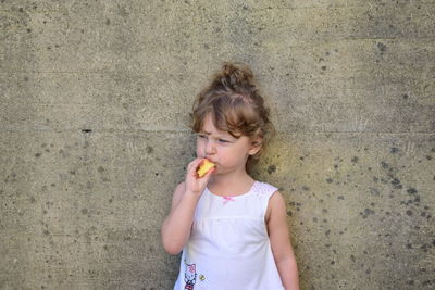Girl eating food while standing against wall