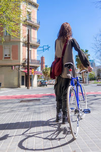 Back view of a smiling woman walking on a city street with bicycle