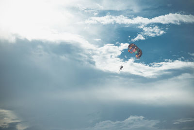 Low angle view of people paragliding against sky